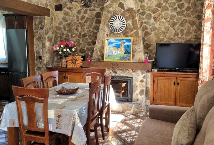 salón con mesa de comedor de madera y sillas, chimenea de piedra, televisión sobre mueble bajo y sofá en primer plano