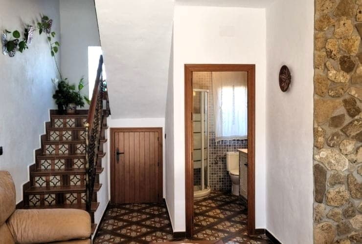 escalera con contrahuellas de azulejos decorados, barandilla de forja, puerta de madera bajo los escalones y baño con plato de ducha y mampara al fondo