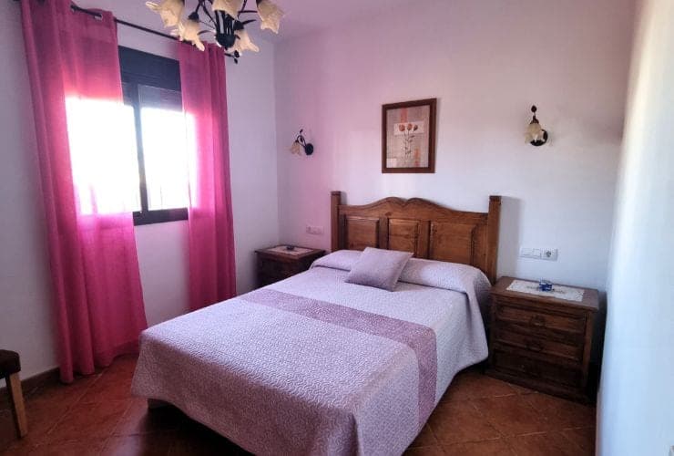 dormitorio con cama de matrimonio de madera, cortinas rosas y lámpara de techo con pantallas de cristal